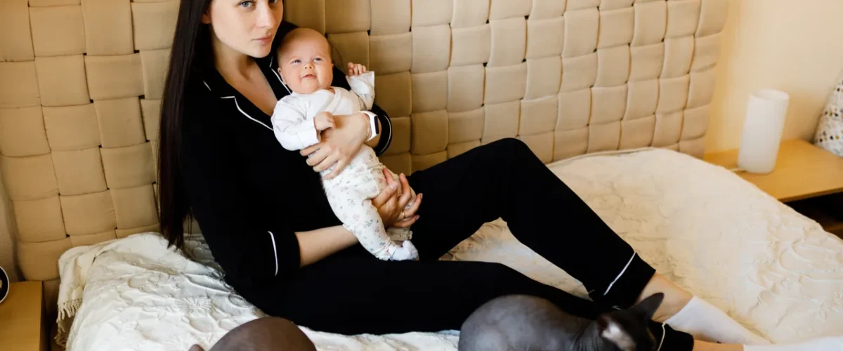 mother with her baby on a bed, pets nearby
