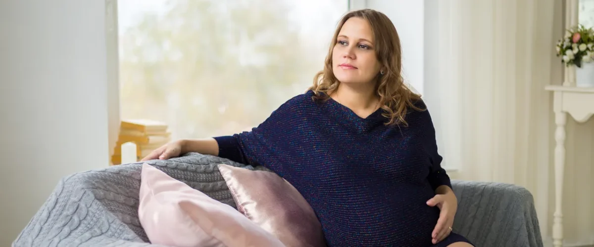 pregnant woman in a navy dress sitting by a large window