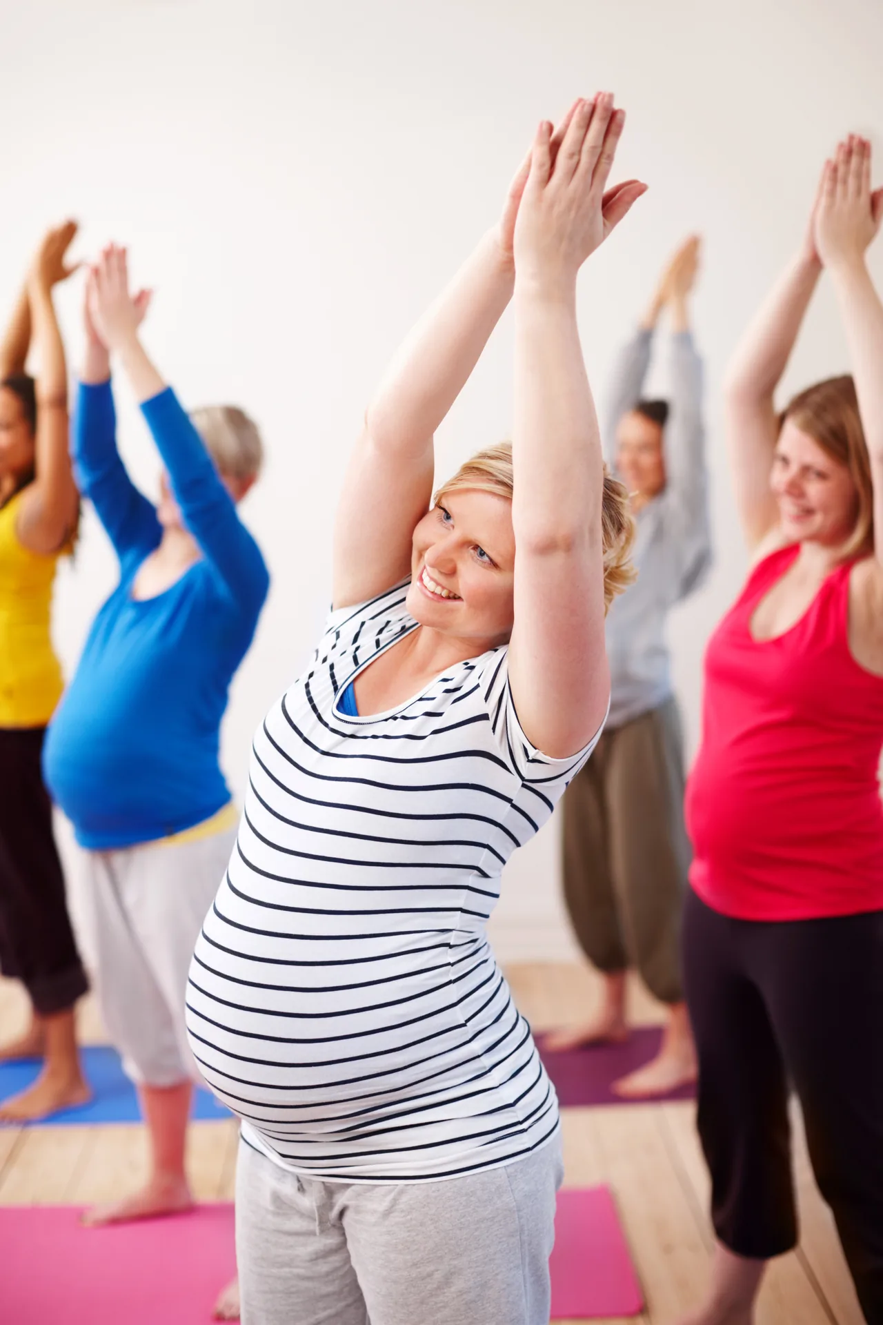 una sala de mujeres embarazadas en una clase prenatal levantando ambos brazos por encima de la cabeza