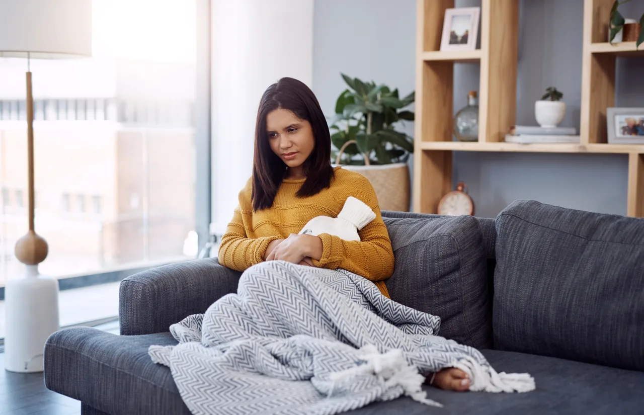 une femme sur le canapé sous un plaid, une bouillotte contre le ventre