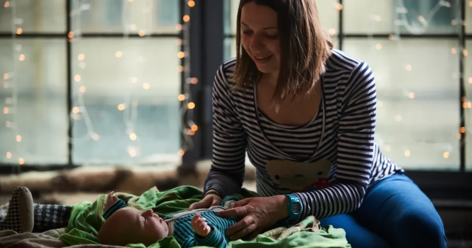 mother tending her baby on a blanket by a window