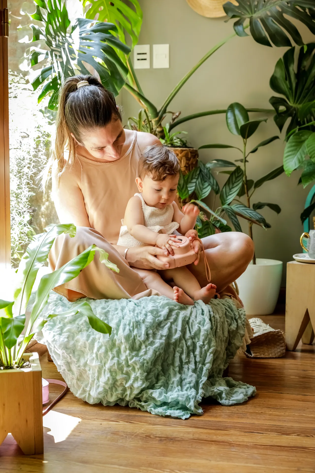 una madre seduta con il figlio di un anno in una stanza piena di piante