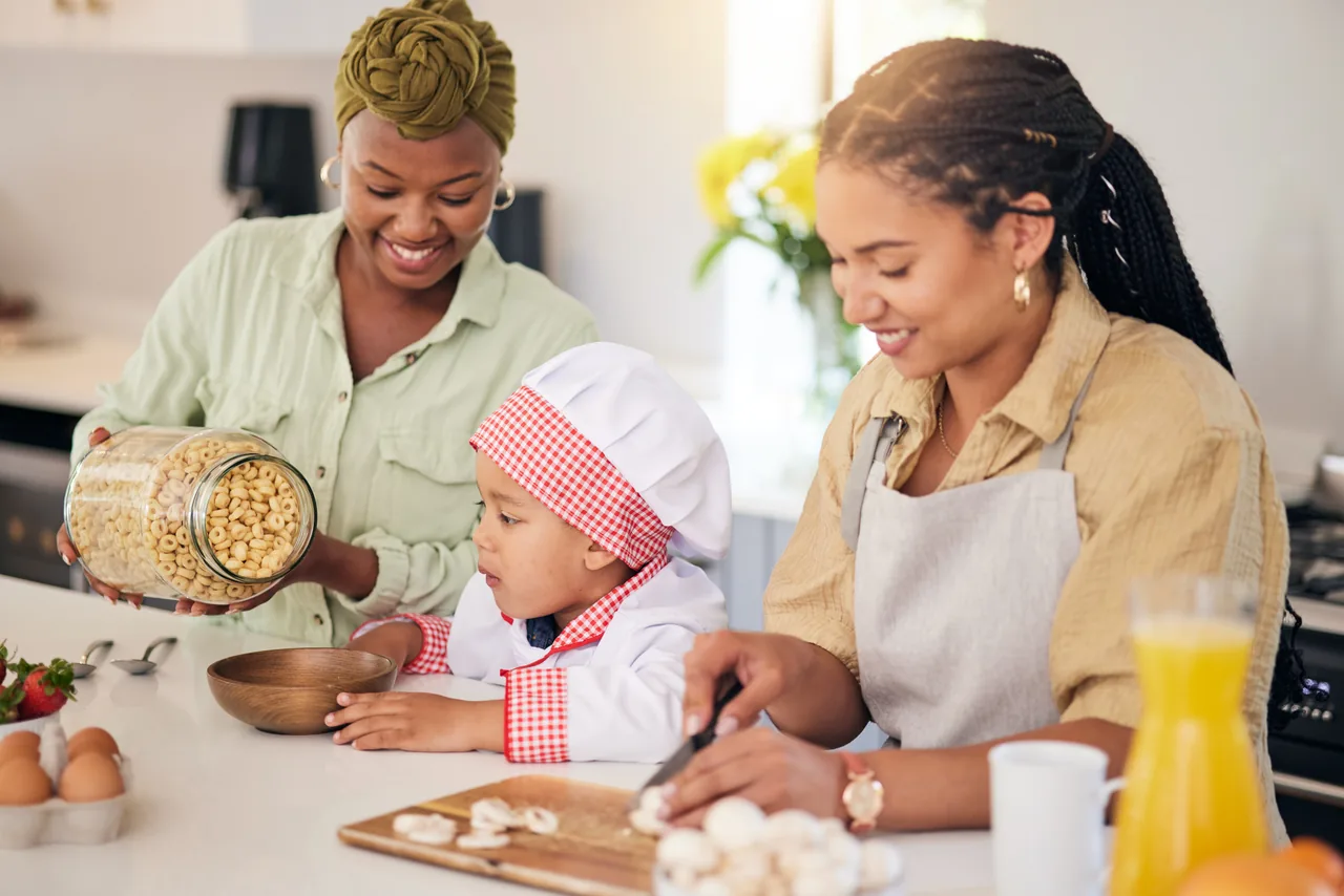 zwei Frauen und ein kleines Kind mit Kochmütze machen gemeinsam an der Kücheninsel Frühstück