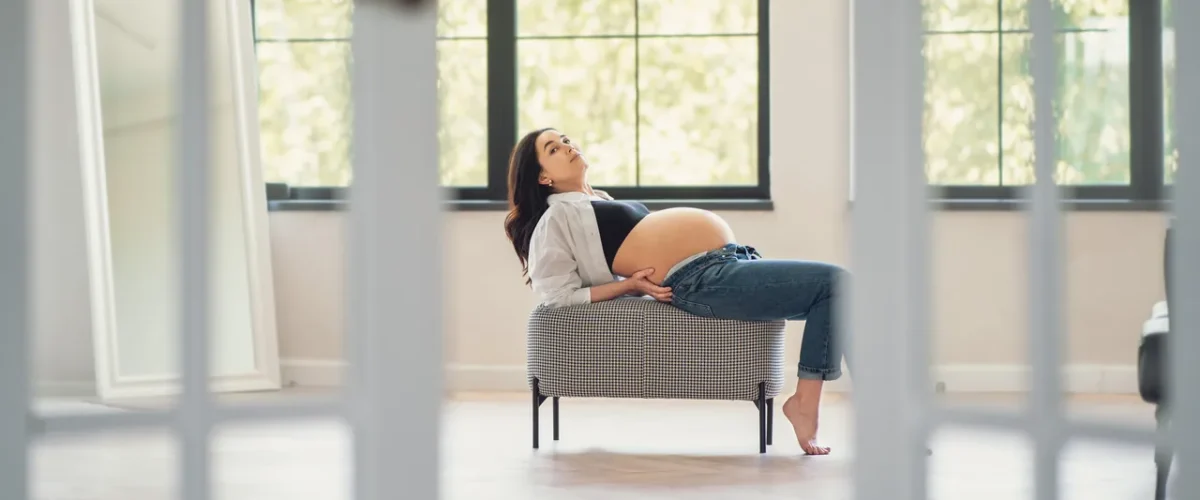 pregnant woman in a white shirt sitting on a bench in a bright airy room