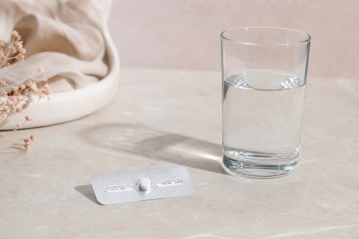 Açık renk tezgâhta bir su bardağının yanında tek beyaz tablet içeren blister